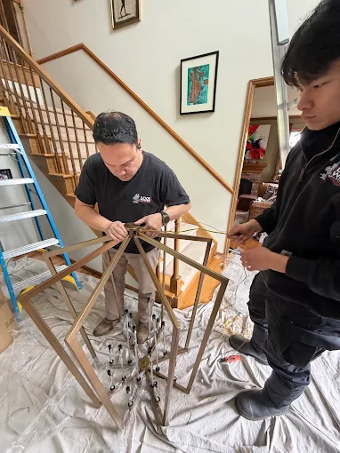 Two Live Wire Electric technicians assembling a chandelier near a staircase