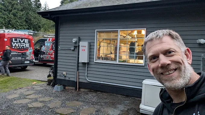 A person smiling for a photo outside a home with Live Wire Electric vans and a standby generator