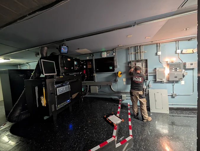 A Live Wire Electric technician at electrical panels beside data equipment