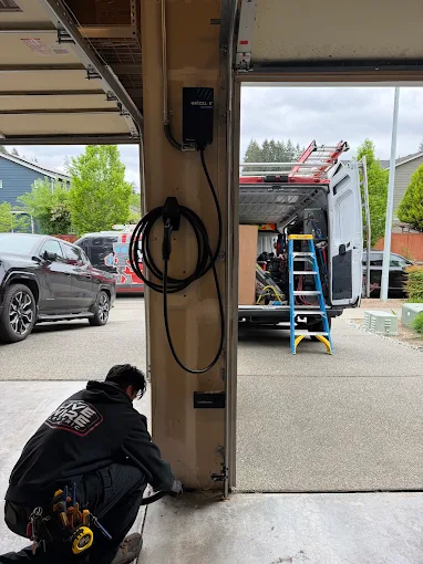 A Live Wire Electric technician working beneath a wall-mounted garage EV charger
