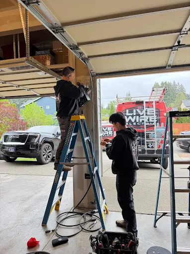 Two Live Wire Electric technicians routing wiring at a garage entrance