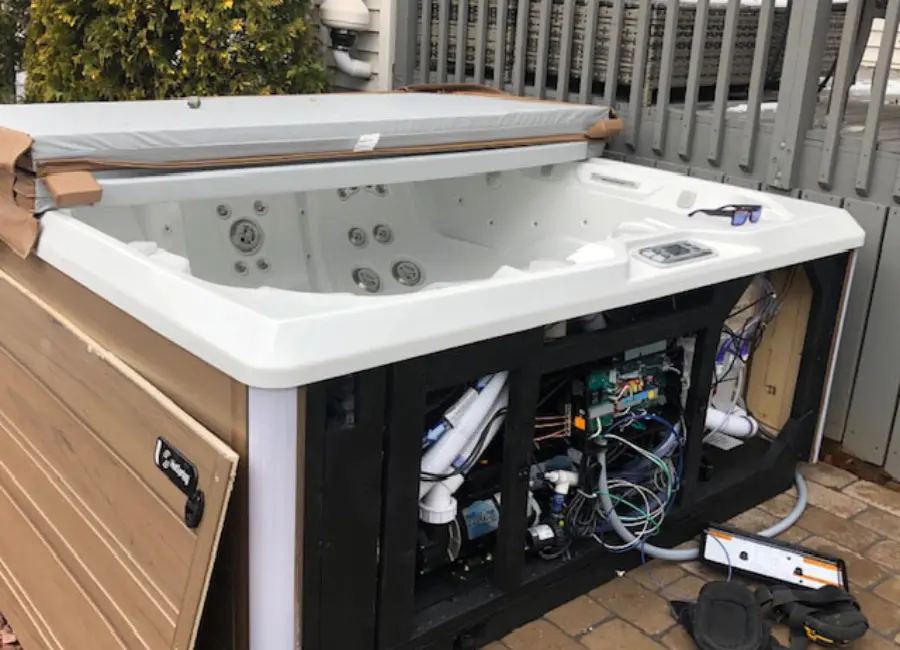Hot tub with its side access panel removed, exposing wiring and equipment.