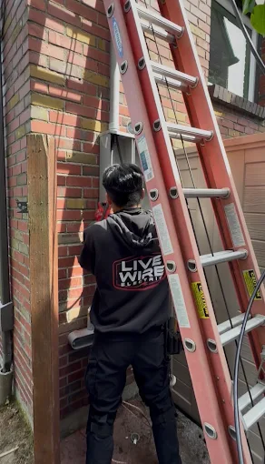 A Live Wire Electric technician working at exterior electrical equipment beside a ladder