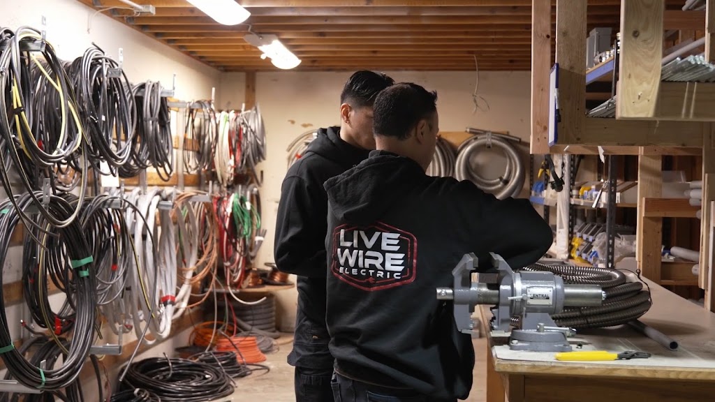 Two Live Wire Electric technicians at a shop workbench beside hanging coils of wire