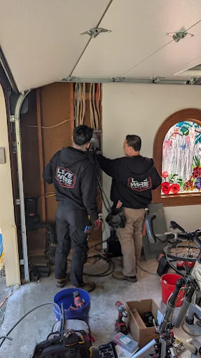 Two Live Wire Electric technicians working on wiring beside an open wall